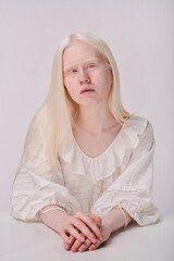 Portrait of young girl having albinism in elegant dress looking at camera against white background
