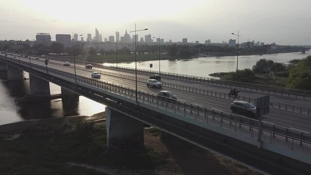 Aerial drone footage of a bridge in Warsaw Poland with traffic flowing and downtown city skyline behind it with bright sun