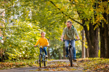Happy father and daughter ride bicycles in autumn park on sunny day.
