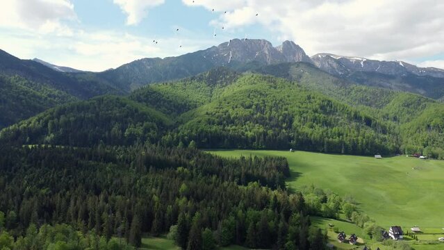Landscape fly by of the legendary Giewont peak in the Polish Tatry Mountains, farmland, forests near Zakopane, Poland, a resort town with traditional Goral architecture. Cloudy summer day green plains