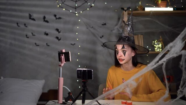 teenage vloger girl records Halloween paper decor on video camera smartphone for blog. mobile phone on tripod, telling blogger for craft videoblog. Technology, art, communication, education
