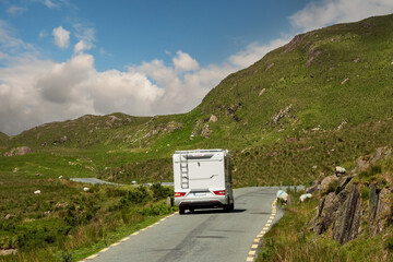 Small motorhome on a small narrow asphalt road in a mountains. Wool sheep grazing grass on the road...