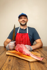 Happy butcher with knife and fresh tomahawk steak on a cutting board. Premium cut of beef. Meat...