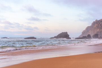Ocean wild beach stormy weather. Praia da Adraga sandy beach with picturesque landscape background,...