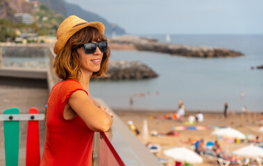 Praia da Calheta in summer, young tourist girl in red dress on the beach, Madeira. Portugal