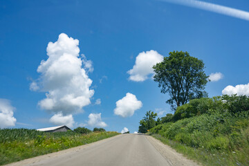road in the countryside go hill with green trees and grass over beautiful blue sky white clouds in summer time.