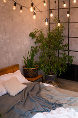 Cozy bedroom area at luxury studio apartment with a free layout in a loft style with big panoramic window and green plant.