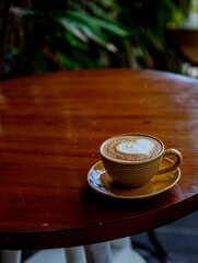 Trendy yellow cup of hot cappuccino on wooden table background. Heart shape latte art for symbol of love.