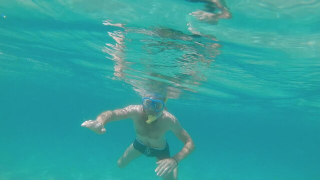 Caucasian bearded man in a mask with a snorkel swims freediving in shallow water in the sea underwater. Snorkeling on a sunny day. waving hands in greeting at the camera