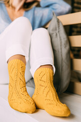 Close up of cozy woman in warm yellow knitted winter socks, white trousers and blue warm sweater resting sitting on a bench at cafe in winter time. Lazy day in knitted socks at cafe. Cozy time.