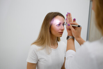 Doctor neurologist shining flashlight on patient eyes to see pupil reaction to light in clinic - obrazy, fototapety, plakaty