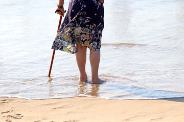 Legs of an elderly person with a cane on the shore of a beach