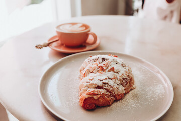 almond croissant and pink cup of cappuccino with latte art in cafe