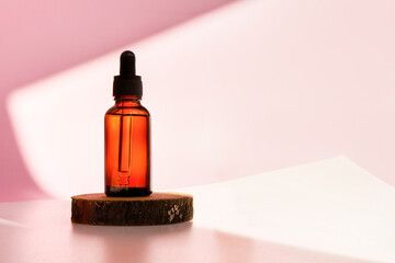 Banner of cosmetic amber glass dropper bottle on wooden podium with oil, serum or fruit peeling in the sunlight. Beauty product presentation, natural pink background. Front view. Mockup concept 