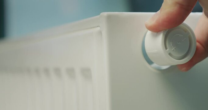 A man's hand regulates the temperature on a heating radiator. Energy Saving