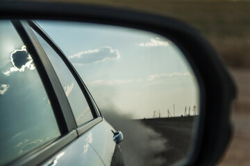 Naklejka premium Reflection of a car in the rearview mirror. Dust behind the car in the side mirror of the car.
