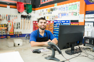 Happy hardware store employee at the computer desk at work - obrazy, fototapety, plakaty