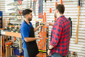 Happy employee showing the tools to a client at the hardware store - obrazy, fototapety, plakaty