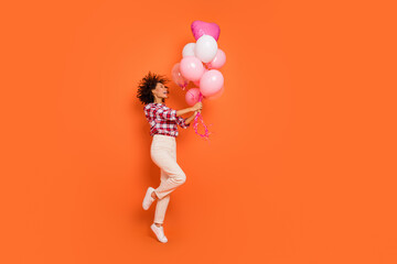 Full length body size view of attractive cheery girl jumping with helium balls festive isolated on bright orange color background
