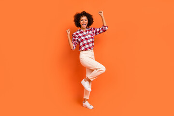 Fototapeta na wymiar Photo of sweet lucky young lady dressed checkered shirt walking rising fists isolated orange color background