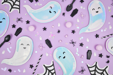 Cute pastel colored Halloween party flat lay with ghost shaped plates, spider web napkins and confetti on violet background