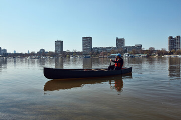 Man paddling in a canoe on a Danube river in urban area, small recreational escape, hobbies and sports outdoors.
