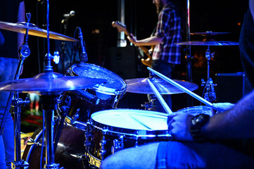 Fototapeta na wymiar Drummer playing drums at stage, close up. Music concert. Drummer on festival with band under the stage lights. Drummer playing drum kit in nightclub at live rock concert. Music instrument.