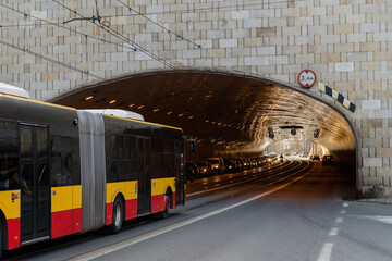 The city long bus drives into the tunnel under the bridge.