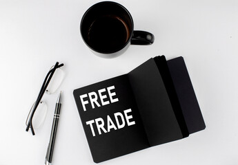 FREE TRADE written text in small black notebook with coffee , pen and glasess on white background. Black-white style