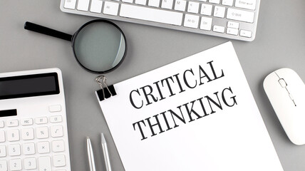CRITICAL THINKING written on paper with office tools and keyboard on the grey background - obrazy, fototapety, plakaty