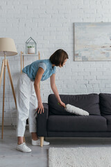 side view of brunette woman cleaning couch in living room at home.