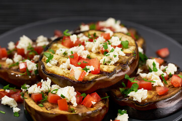 close up homemade eggplant salad with cheese and tomatoes, on a black table.