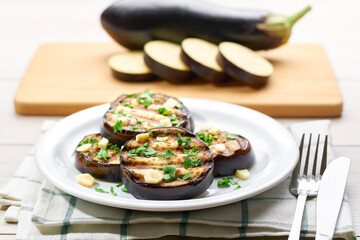 Salad with grilled eggplant, parsley and garlic on a white plate,selective focus.whole eggplant background.
