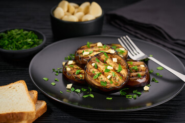 homemade eggplant salad with parsley and garlic on a black table.