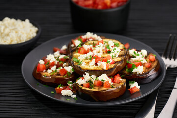 Homemade grilled eggplant with feta and tomatoes on a black table.