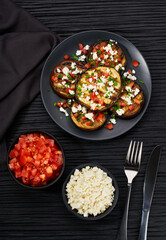 Homemade grilled eggplant with feta and tomatoes on a black table, top view.