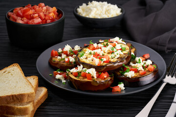 Homemade grilled eggplant with feta and tomatoes on a black table.