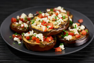 Salad with grilled eggplant, feta and tomatoes on a black plate,selective focus.