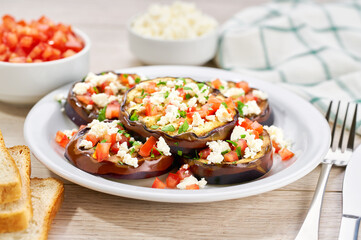 Homemade grilled eggplant with feta and tomatoes on a white table.