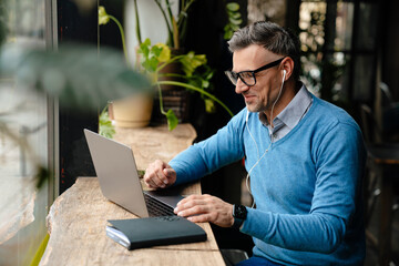 Adult smiling man in glasses and headphones working with laptop