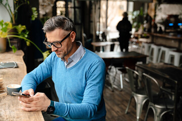 Mid white man using mobile phone while drinking coffee at cafe