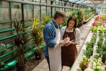 White woman and man wearing aprons standing by plants in greenhouse