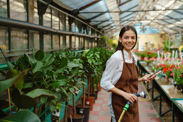 Naklejka na ściany i meble White woman wearing apron using cellphone while working in greenhouse