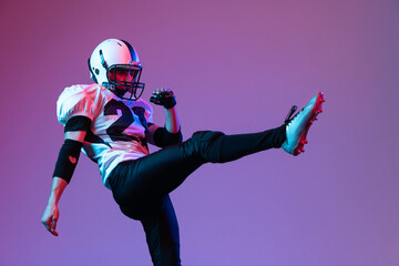 Portrait of young man, american football player in uniform posing isolated over purple background in neon light. © Lustre Art Group 