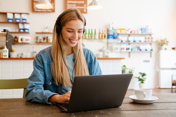 White blonde woman listening music while working with laptop in cafe