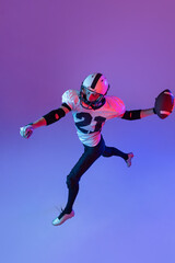 Top view portrait of man, american football player training isolated over purple background in neon light. Action