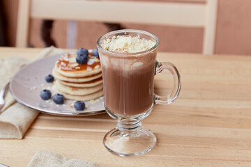 Sweet belgian chocolate with ice cream in glass and traditional pancakes with syrup and blueberry on the wooden table. Delicious breakfast in the cafe.
