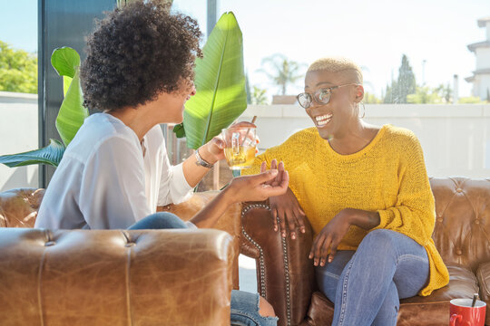 Positive African American woman speaking with friend sitting on couch at home during weekend