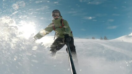 A snowboarder rides through deep snow and turns in the fresh powder. Snow splashes into the camera and athlete. Winter sports activities on a sunny winter day.
