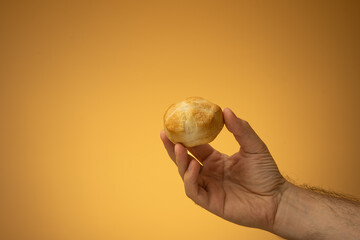 Homemade oven backed small panini bun held in hand by Caucasian male hand. Close up studio shot,...